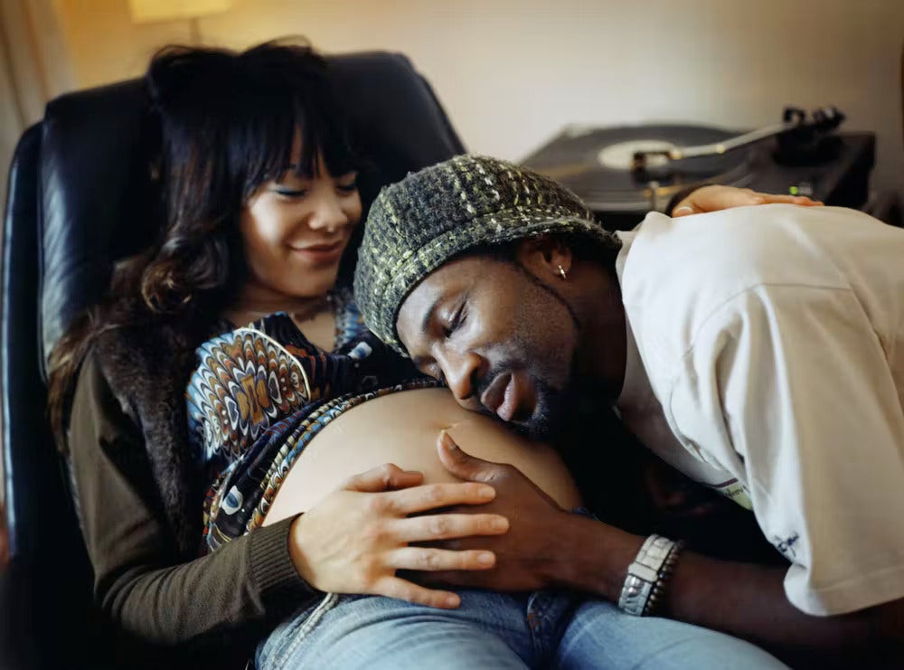 Black man listens to Black pregnant woman's belly
