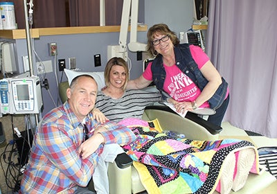 Michelle Brubaker in a hospital bed with her husband and mom surrounding her