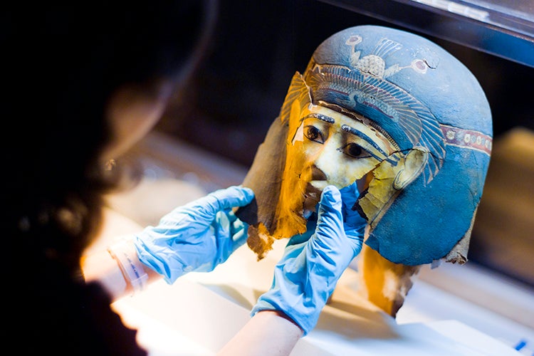 Gloved hands hold an Egyptian mask