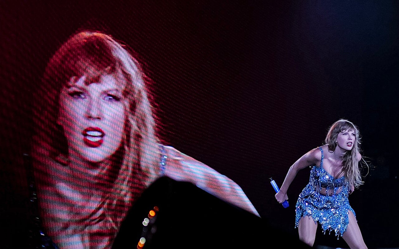 Taylor Swift performs in a sequined dress in front of an image of herself on a giant screen