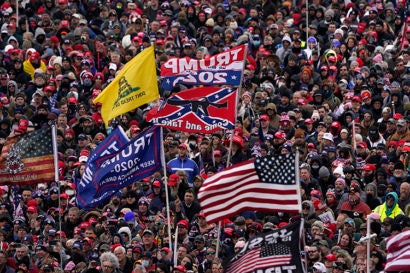 A large crowd in Washington DC. In the foreground are five flags: the American Flag, 2 Trump campaign flags, the Don't Tread On Me Flag, and a Confederate flag.