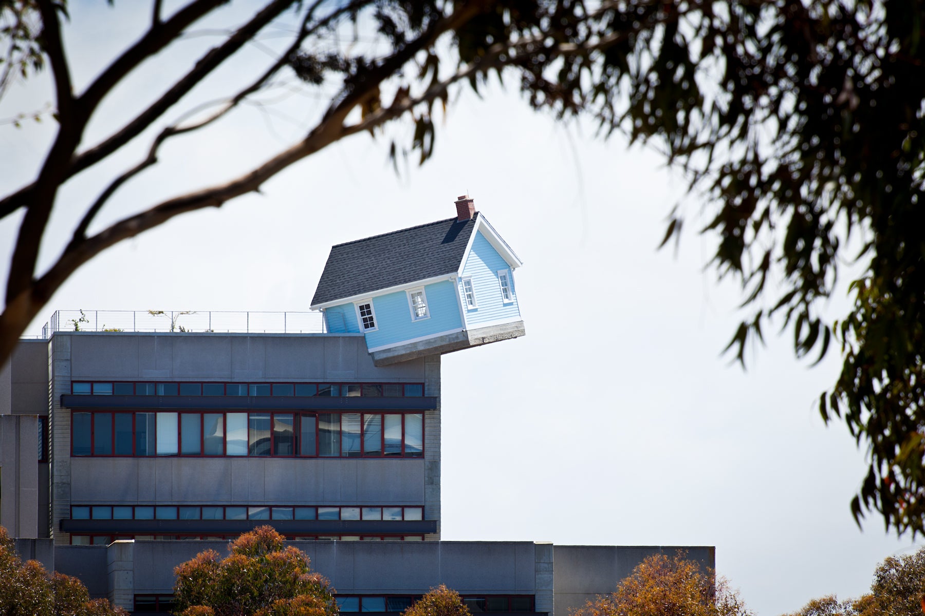 A small house seems to balance on the edge of a large building