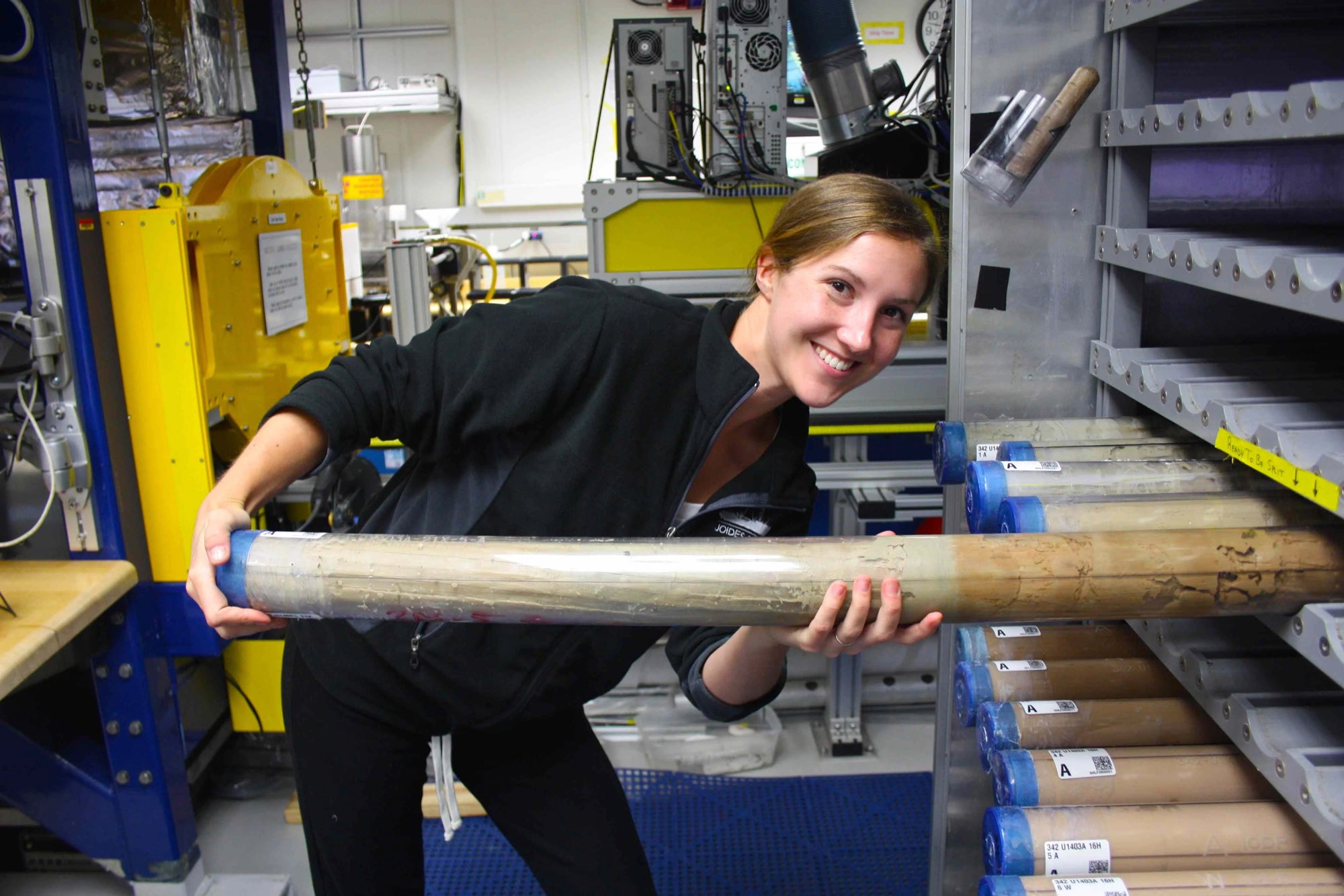 Blonde woman, smiling, pulls a long canister out of a cabinet