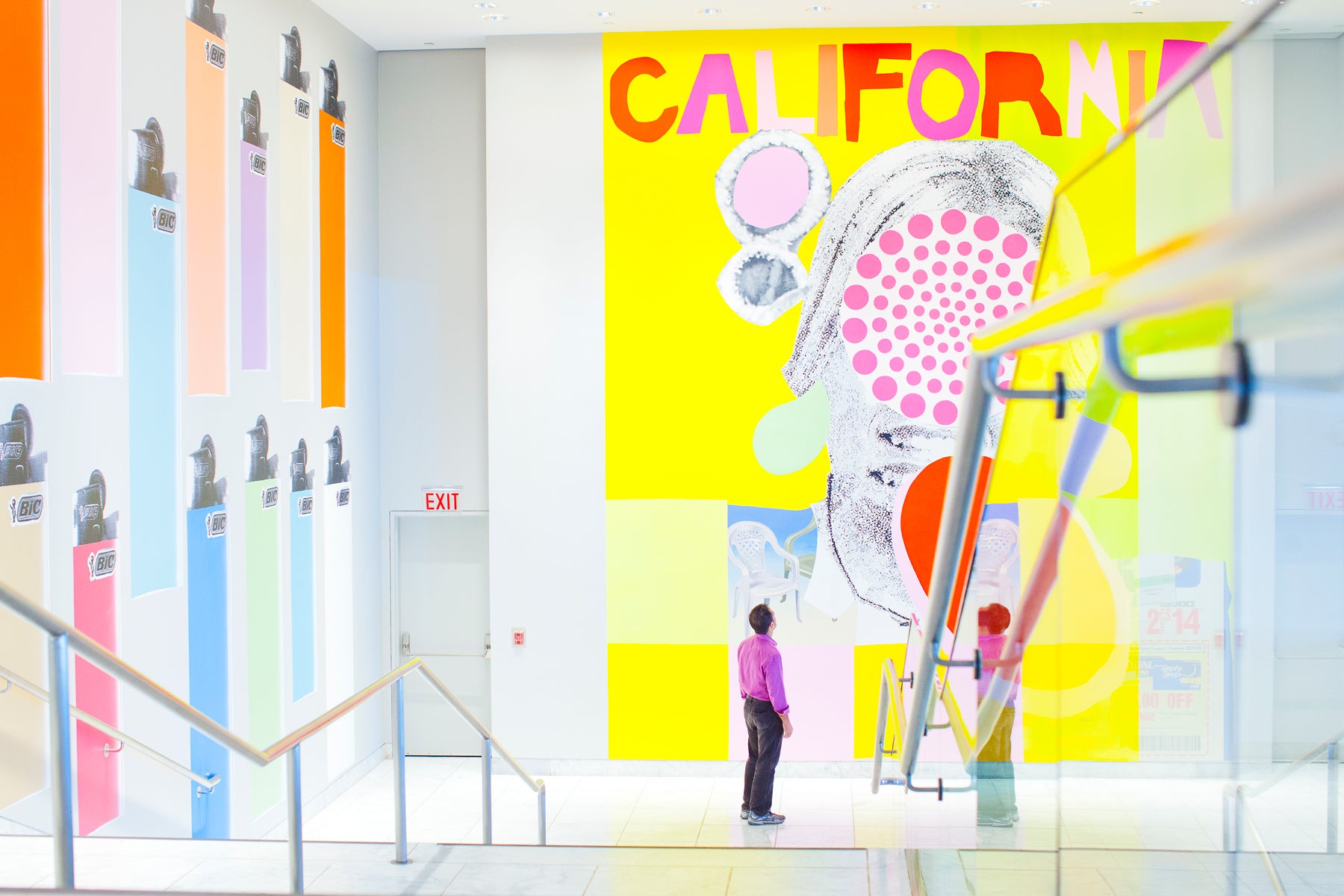 A person standing at the bottom of a stairway inside a building looking up at a mural