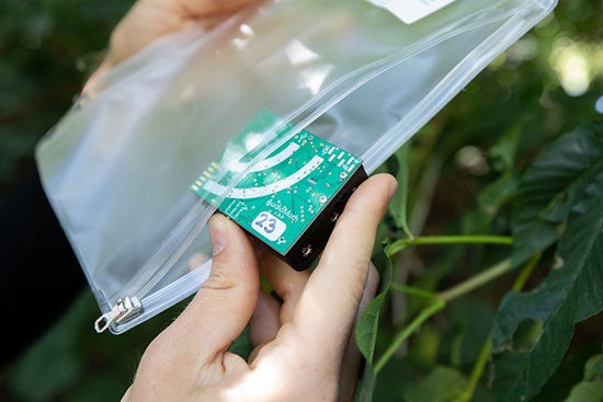 A hand takes a device about half the size of a credit card out of a plastic bag
