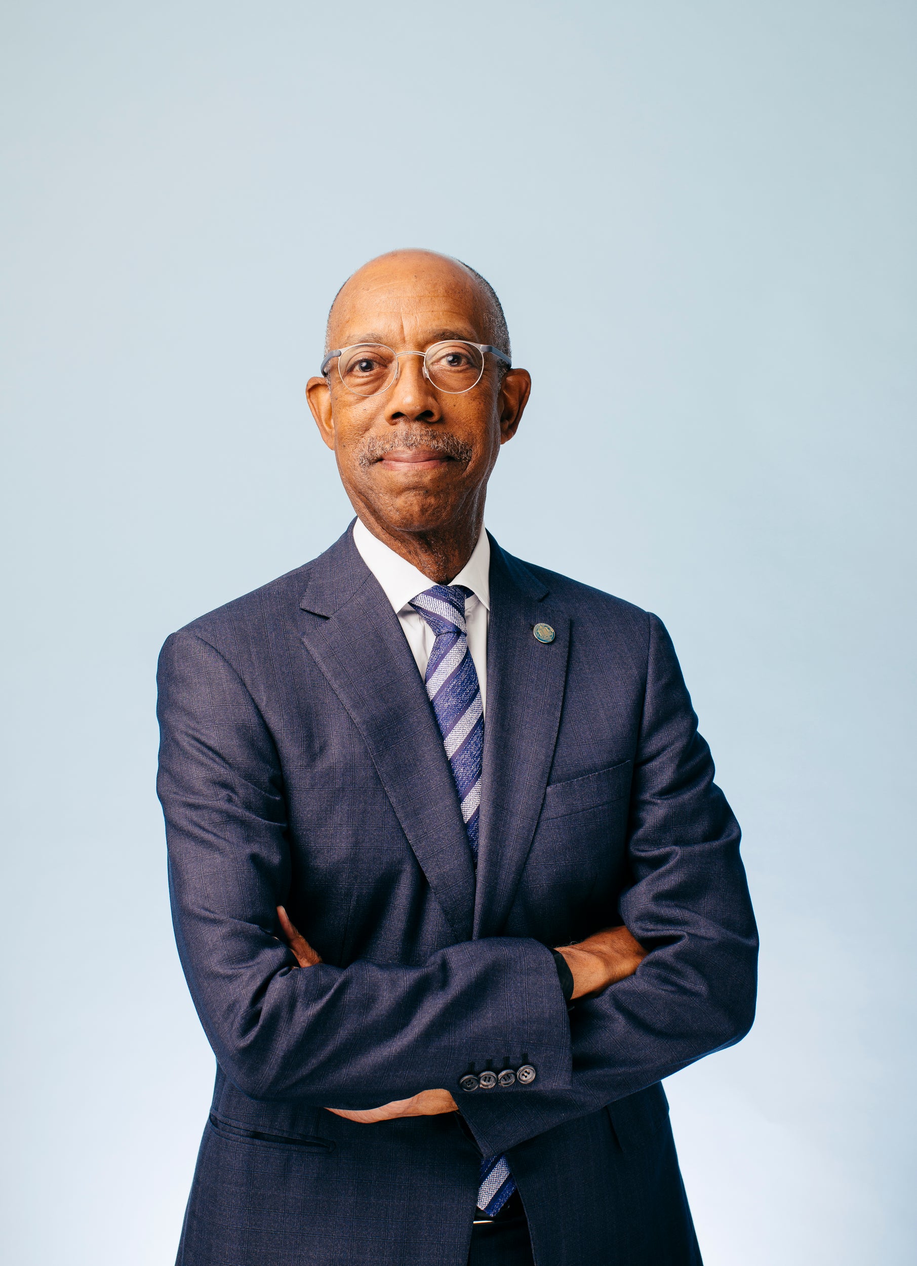 Michael V. Drake, M.D., smiling man with glasses, in a navy suit, arms folded