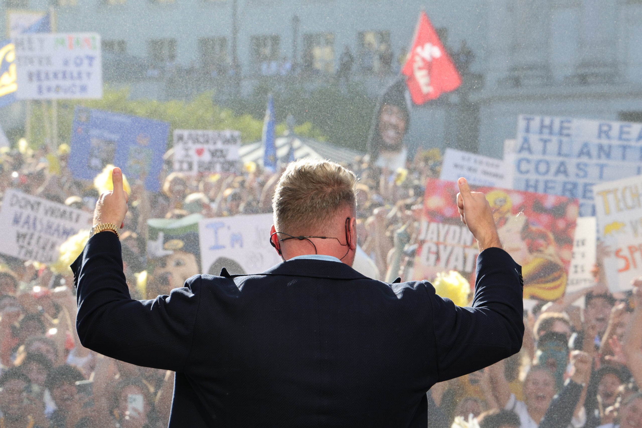 View of a a man with arms raised hyping up a giant crowd of UC Berkeley students with signs in early morning light in front of Doe Library