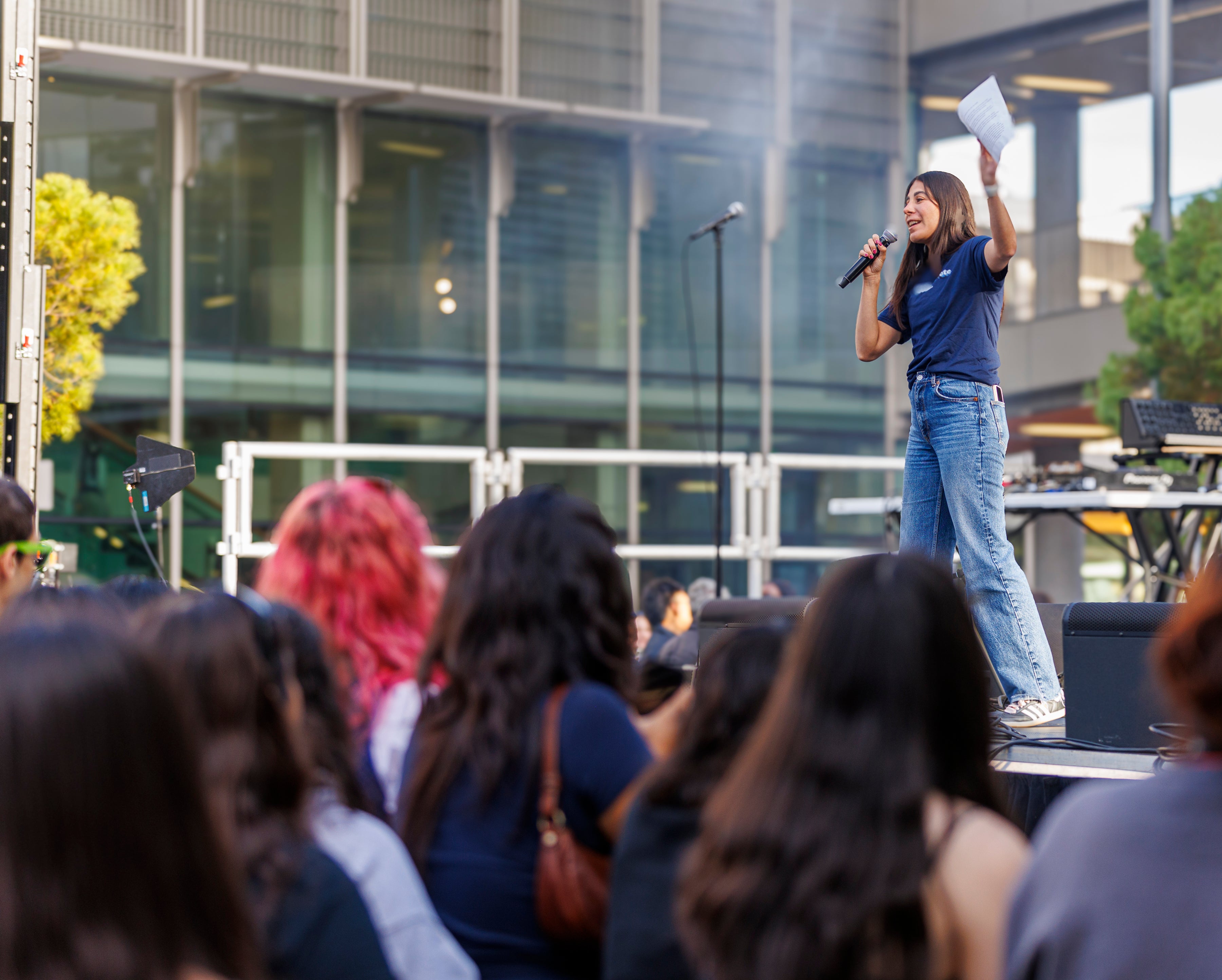 A student wearing a GO BEARS. GO VOTE. t shirt stands on a stage in Sproul Plaza, speaking into a microphone and gesticulating, in front of a crowd
