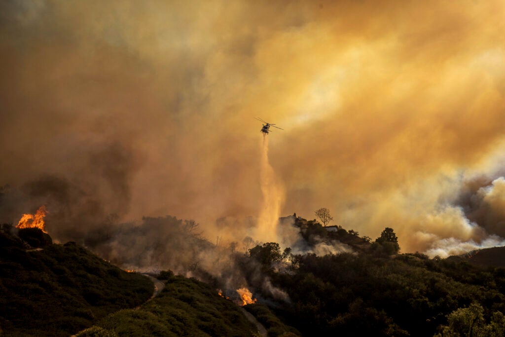 A helicopter drops water on a wildfire