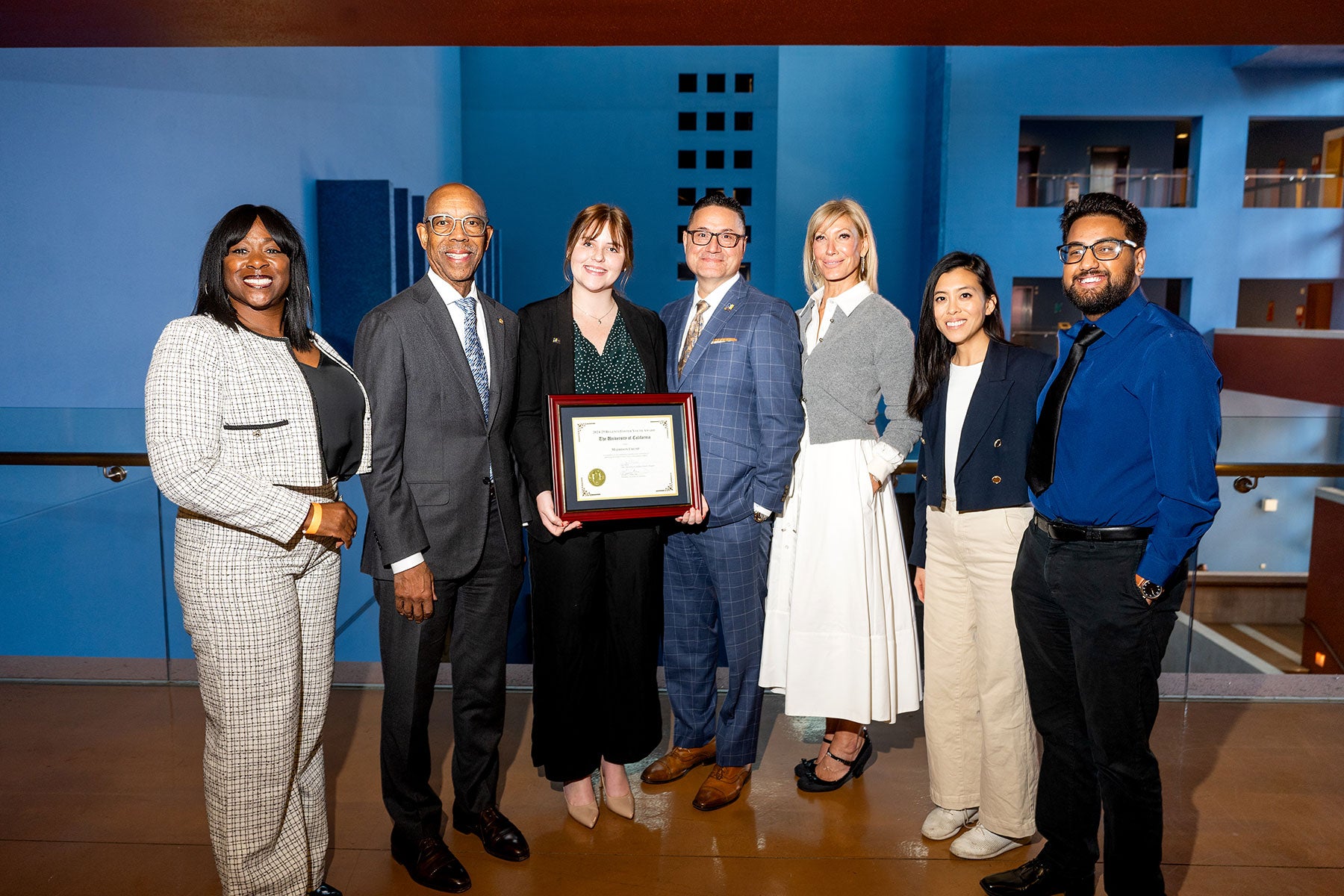 Maddison Crump holds a plaque and poses for a photograph with UC Student Regent Designate Sonya Brooks, UC President Michael Drake, UC Merced Chancellor Juan Sánchez Muñoz, UC Regent Chair Janet Reilly and UC Student Regent Josiah Beharry.  