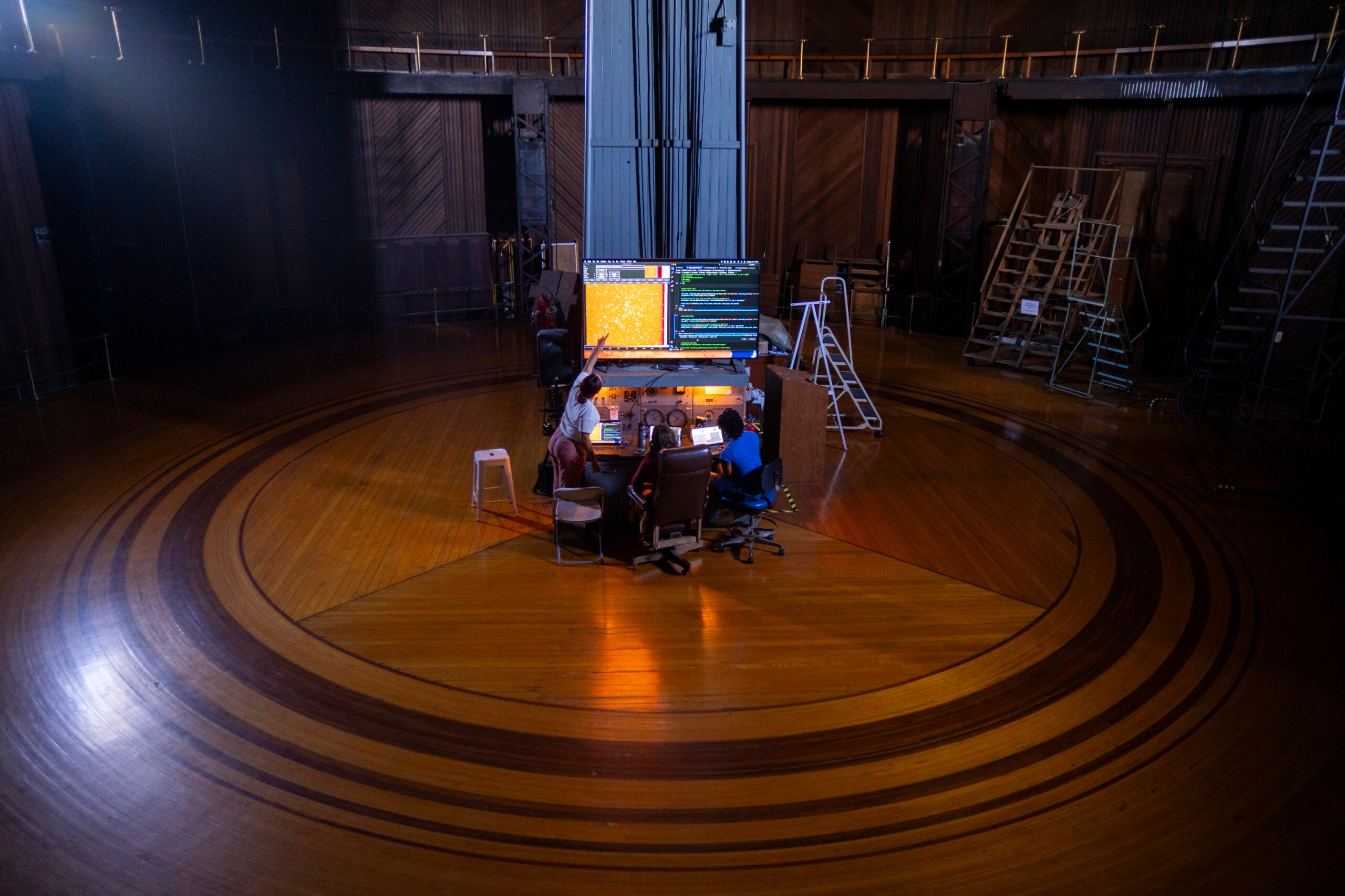 A tall, complex machine in the middle of a room with a circular design in its wooden flooring.