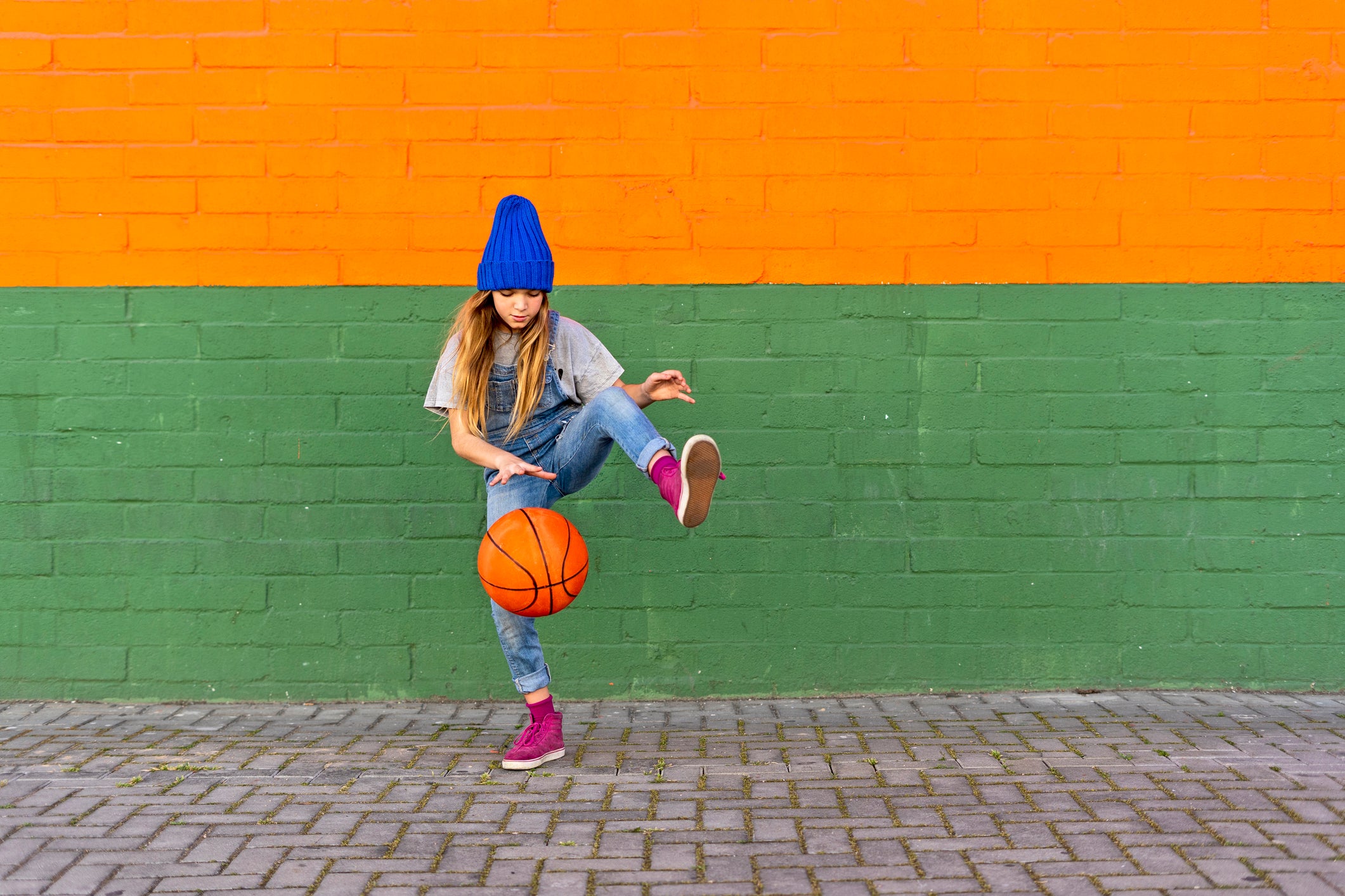 A girl bouncing a basketball against a colorful wall