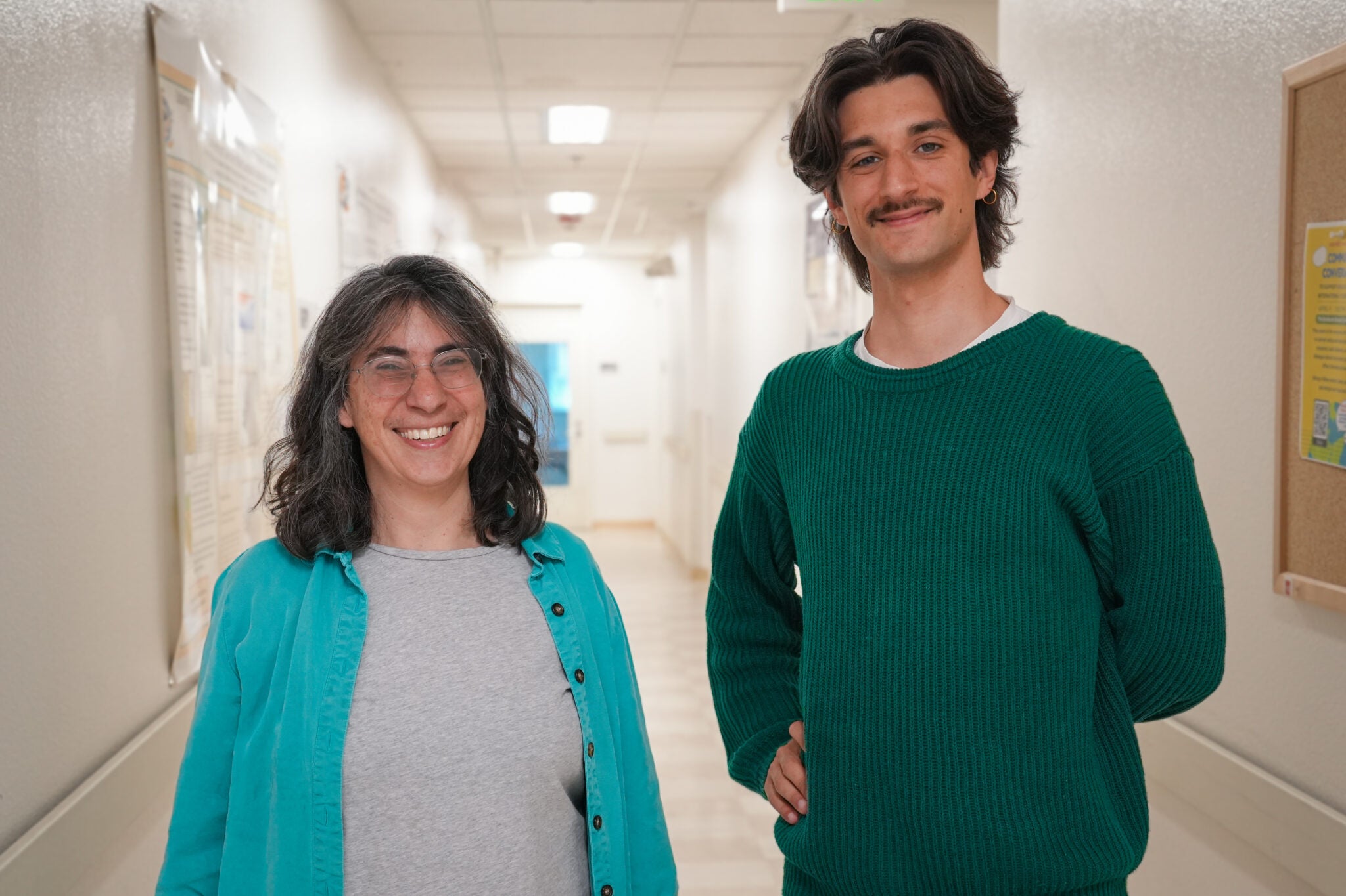 Two researchers, a woman with glasses and shoulder length hair on the left, and a taller young man with a mustache on the right
