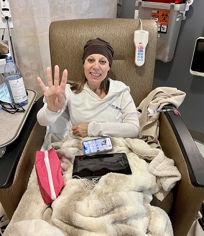 A woman in a medical chair under blankets waves