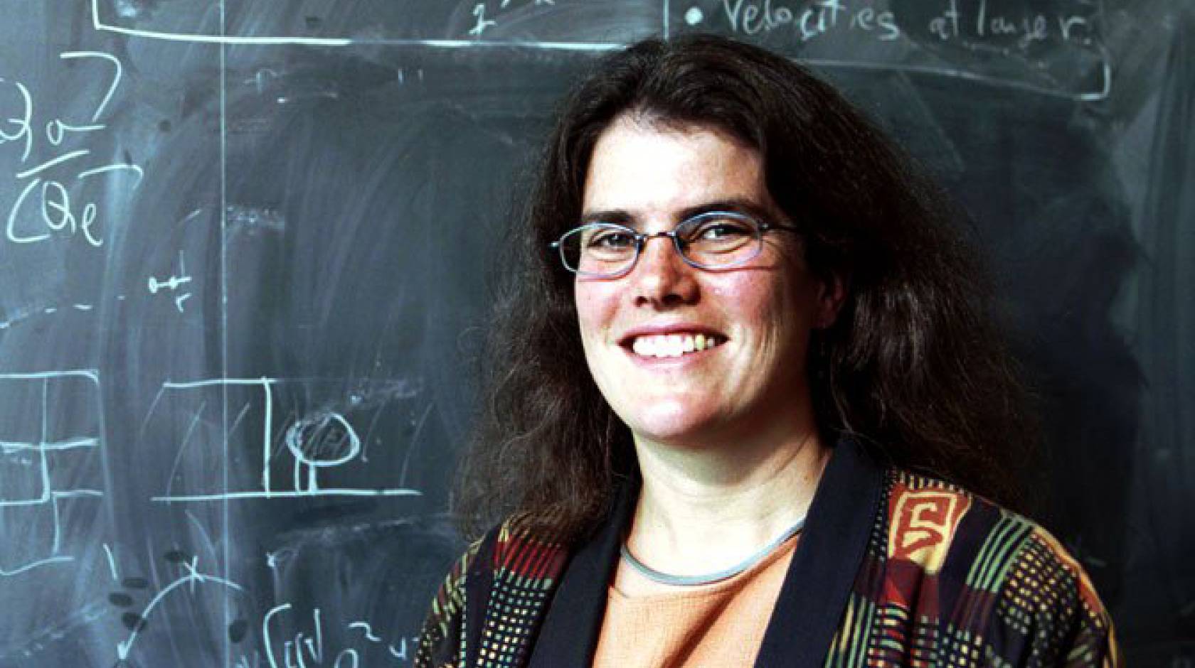 Andrea Ghez smiles in front of a chalkboard