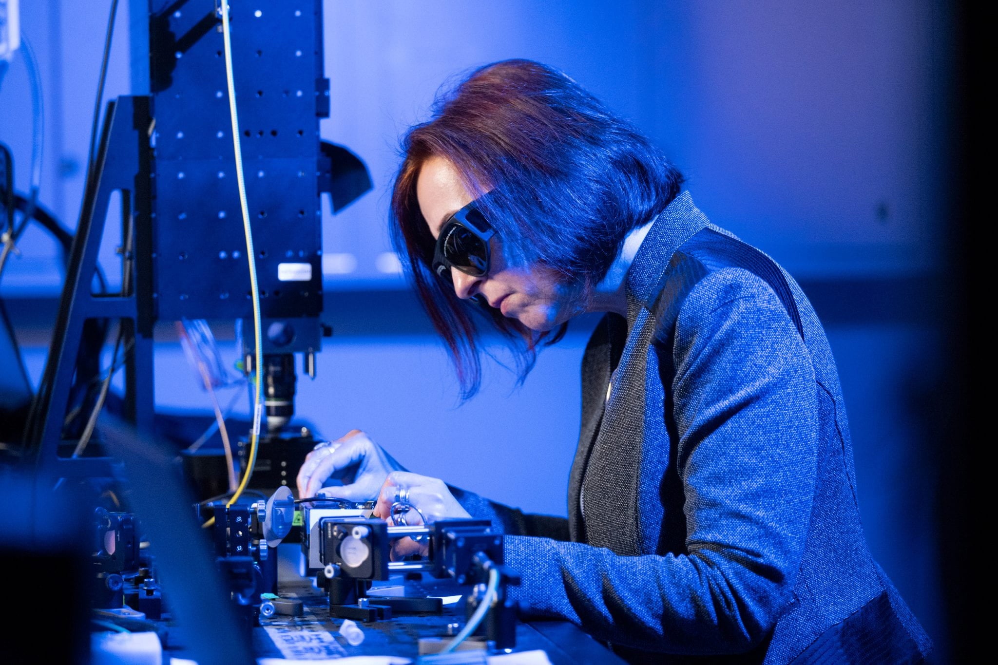 A woman wearing protective goggles uses a complex piece of lab equipment