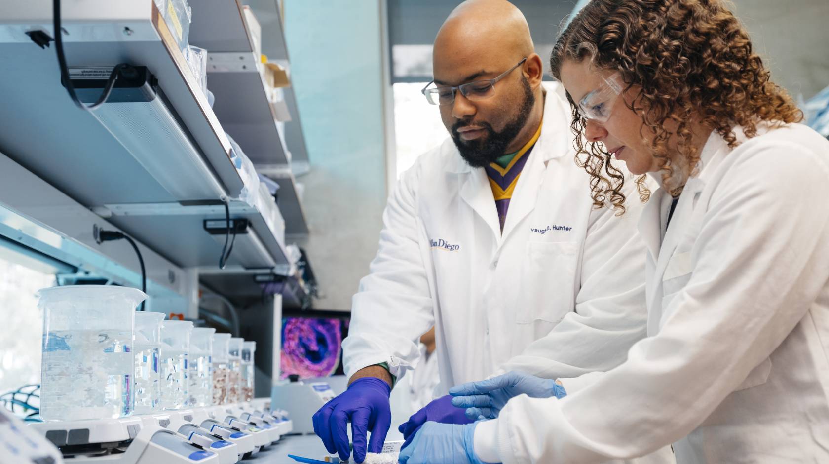 Two scientists in white lab coats work together in a laboratory.