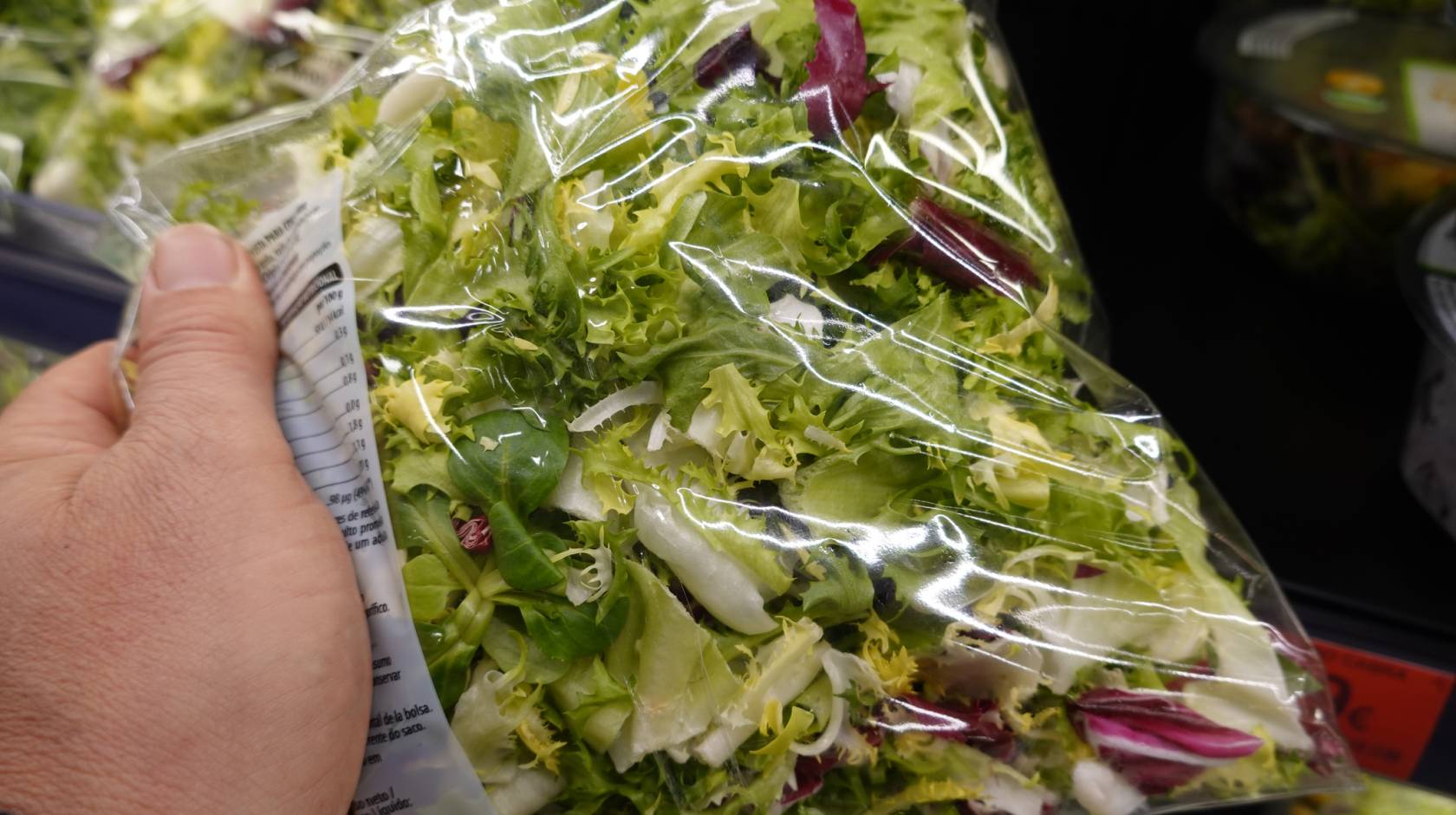A hand holds a bag of salad greens at a grocery store