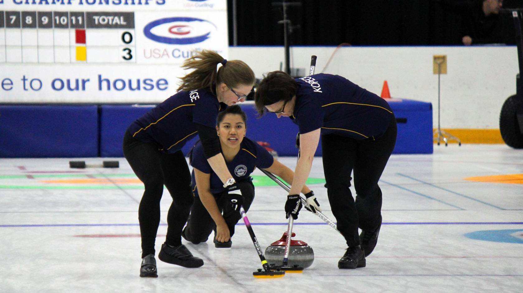 Three women curling, one delivering the stone, two sweeping