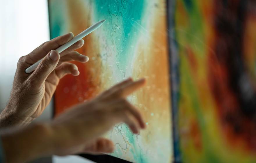 Hands using a stylus and finger to interact with a large touchscreen displaying a colorful weather map