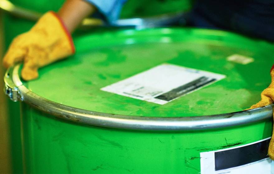 Yellow-gloved hands hold a chemical barrel