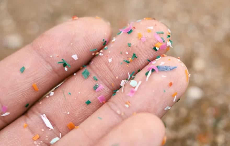 Close-up of a person's upturned palm and fingers with tiny shards of multi colored plastic stuck to the skin.