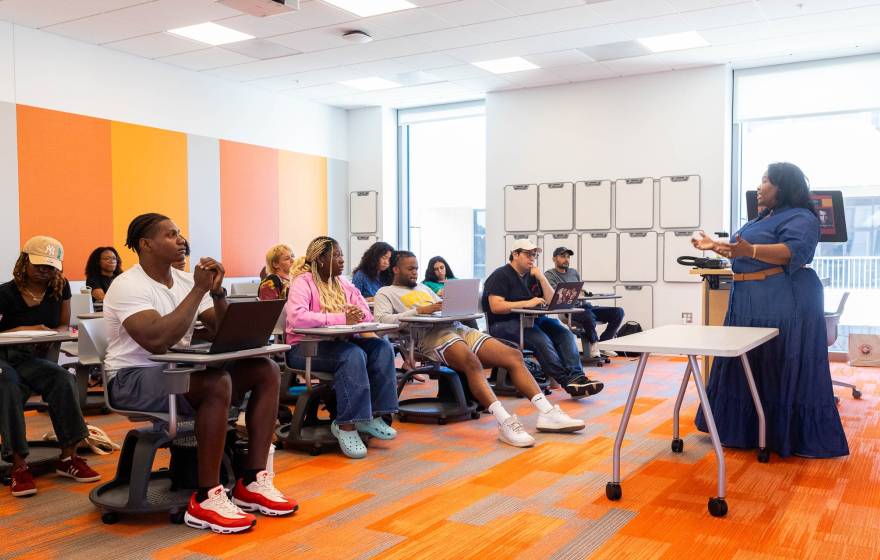 A teacher lectures before a class of students seated at desks