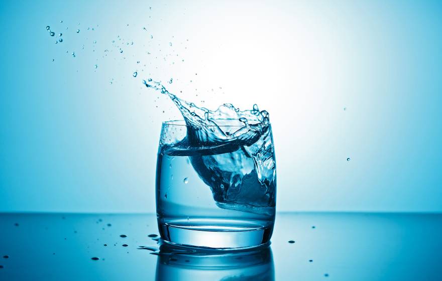 A glass of water with some water splashing out on a blue background