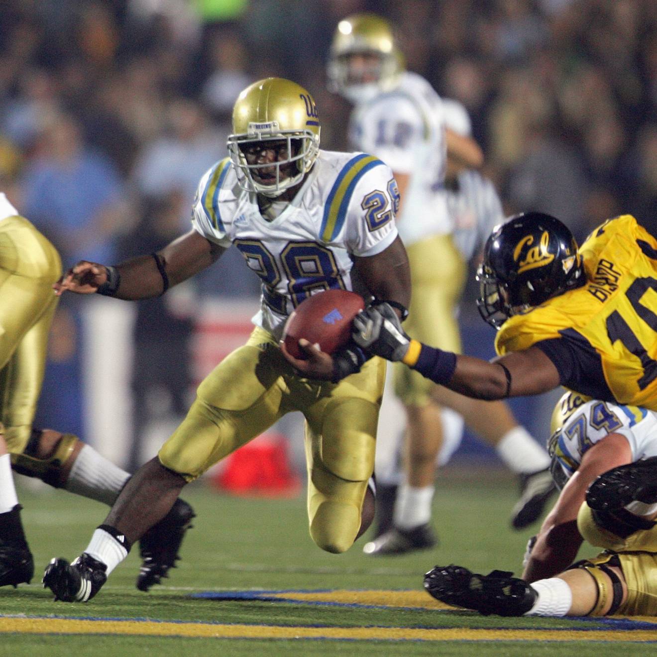 A UCLA football player carries the ball past a diving Cal player while another UCLA player blocks to his right