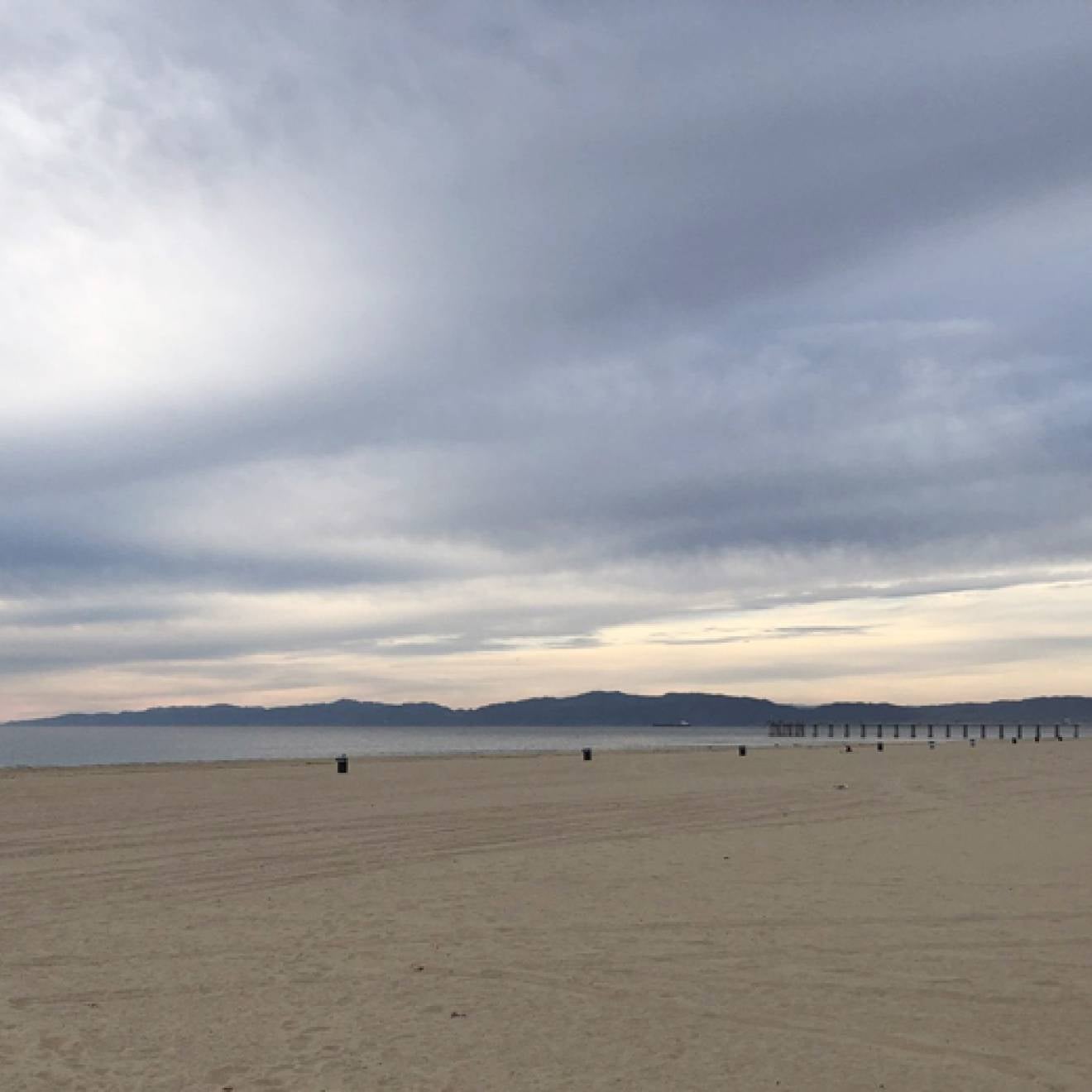 A wide-angle view of Hermosa Beach under a dramatic, cloudy sky